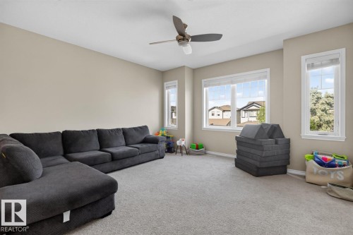 Spacious room featuring neutral paint, gray carpet flooring, multiple windows with white trim, and a ceiling fan with integrated lighting - 109 Selkirk Place, Leduc, AB - Indoor Photo Showing Living Room