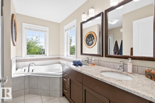 Bathroom featuring a built-in corner tub with tiled surround, dual windows, a double vanity with granite countertop, two undermount sinks, and two framed mirrors - 109 Selkirk Place, Leduc, AB - Indoor Photo Showing Bathroom