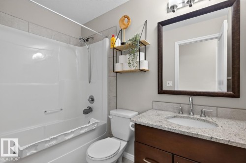 Bathroom featuring a white tub-shower combination with tiled surround, a dark wood-finish vanity with a light-toned countertop, and a rectangular framed mirror - 109 Selkirk Place, Leduc, AB - Indoor Photo Showing Bathroom
