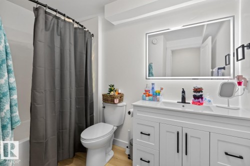 Bathroom featuring a white vanity with integrated sink, a rectangular LED-backlit mirror, wood-finish flooring, and a white toilet - 109 Selkirk Place, Leduc, AB - Indoor Photo Showing Bathroom