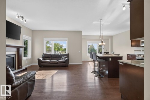 Open-concept living space featuring wood-finish flooring, a fireplace with a wood mantel, and multiple windows - 109 Selkirk Place, Leduc, AB - Indoor Photo Showing Living Room With Fireplace