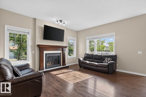 Spacious living area featuring rich wood-finish flooring, a prominent fireplace with a dark wood mantel and tile surround, and multiple large windows - 109 Selkirk Place, Leduc, AB - Indoor Photo Showing Living Room With Fireplace