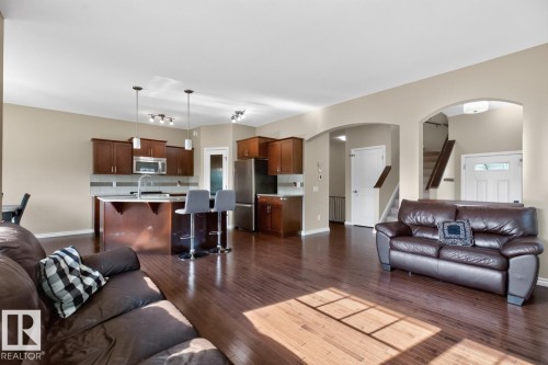 Open-concept living area featuring rich wood-finish flooring, a kitchen island with pendant lighting, stainless steel appliances, and arched doorways - 109 Selkirk Place, Leduc, AB - Indoor Photo Showing Living Room