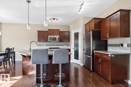 Kitchen featuring wood-finish flooring, dark wood cabinetry, stainless steel appliances, and a central island with a sink and pendant lighting - 109 Selkirk Place, Leduc, AB - Indoor Photo Showing Kitchen
