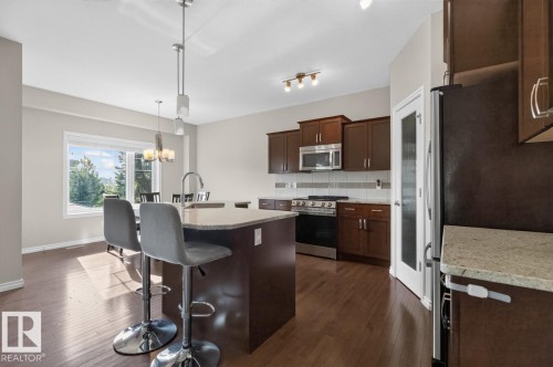 Open-concept kitchen featuring an island with a breakfast bar, rich wood-finish flooring, dark wood cabinetry, and stainless steel appliances, including a microwave and range - 109 Selkirk Place, Leduc, AB - Indoor Photo Showing Kitchen