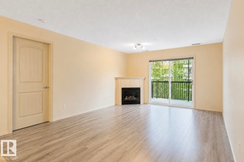 Living area featuring wood-finish flooring, a corner fireplace with a mantel, and light-toned walls - #203 17407 99 Av Nw, Edmonton, AB - Indoor Photo Showing Living Room With Fireplace