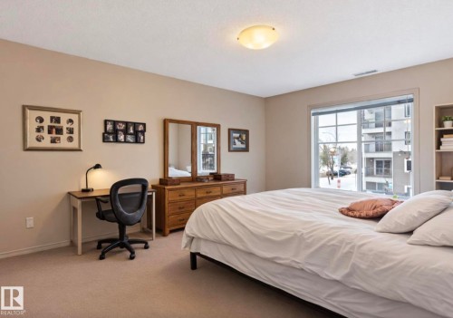 Carpeted bedroom with a large window, neutral wall tones, and a built-in shelving unit - #203 17407 99 Av Nw, Edmonton, AB - Indoor Photo Showing Bedroom