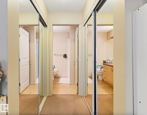 Hallway with mirrored bi-fold closet doors and carpet flooring - #203 17407 99 Av Nw, Edmonton, AB - Indoor