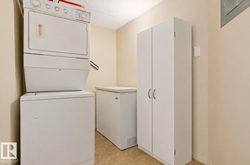 Dedicated laundry area featuring a stacked washer and dryer, adjacent to a chest freezer and a tall storage cabinet - #203 17407 99 Av Nw, Edmonton, AB - Indoor Photo Showing Laundry Room