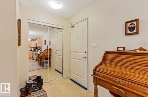 Entryway featuring light-toned tile flooring, a white paneled door with brushed nickel hardware, and a mirrored closet with sliding doors - #203 17407 99 Av Nw, Edmonton, AB - Indoor Photo Showing Other Room
