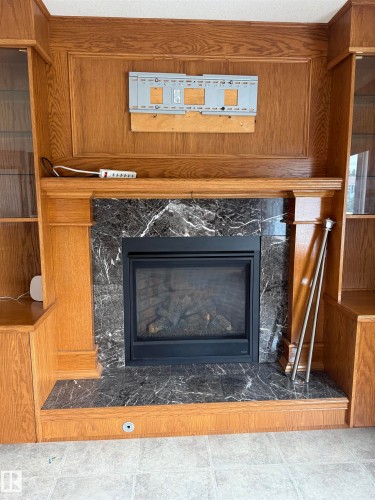 Central fireplace with a black insert, dark stone surround, and wood-finish mantel - 1412 63 Street Nw, Edmonton, AB 