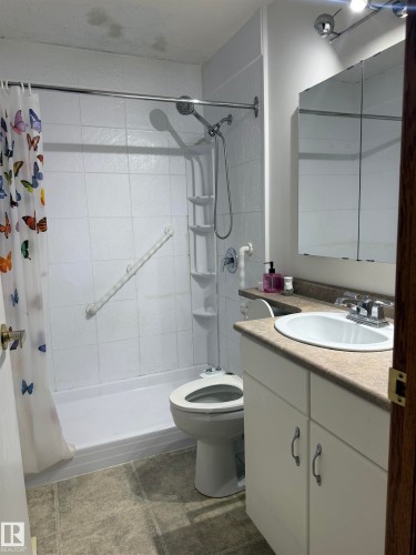 Shower-tub combination with white tile surround, single vanity with integrated sink, track lighting, and mirrored medicine cabinet - 1412 63 Street Nw, Edmonton, AB 