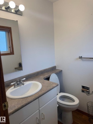 White vanity cabinet with an integrated sink, laminate countertop, and wood-finish flooring - 1412 63 Street Nw, Edmonton, AB 