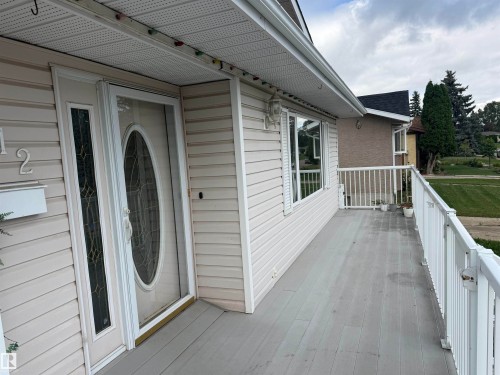 Exterior featuring light-toned siding, a full-light entry door with decorative glass, and a porch with white railings - 1412 63 Street Nw, Edmonton, AB 