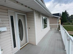Exterior featuring light-toned siding, a full-light entry door with decorative glass, and a porch with white railings - 