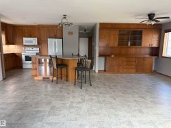 Tile flooring throughout, extensive wood-finish cabinetry, built-in kitchen island with countertop, integrated white appliances, and ceiling fan - 