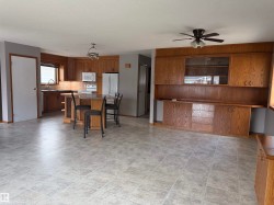 Expansive room featuring a kitchen area with wood cabinetry, a kitchen island with a stone-finish countertop, and a built-in wall unit with wood cabinetry - 