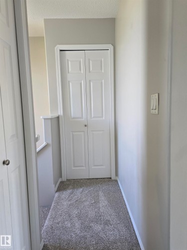 Hallway featuring light gray walls, textured carpet flooring, and white bi-fold doors - 4120 47 Street, Drayton Valley, AB - Indoor Photo Showing Other Room