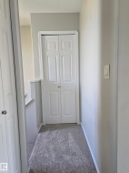 Hallway featuring light gray walls, textured carpet flooring, and white bi-fold doors - 