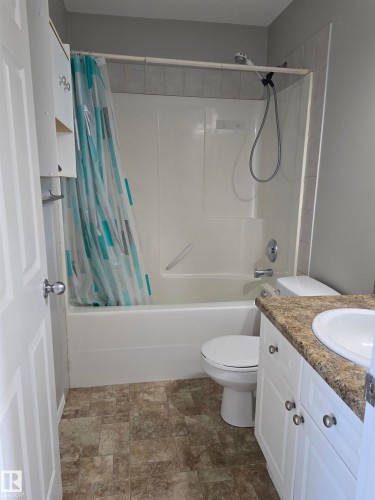 Bathroom featuring a white bathtub with shower, white toilet, white vanity with integrated sink, patterned countertop, and light-toned flooring - 4120 47 Street, Drayton Valley, AB - Indoor Photo Showing Bathroom