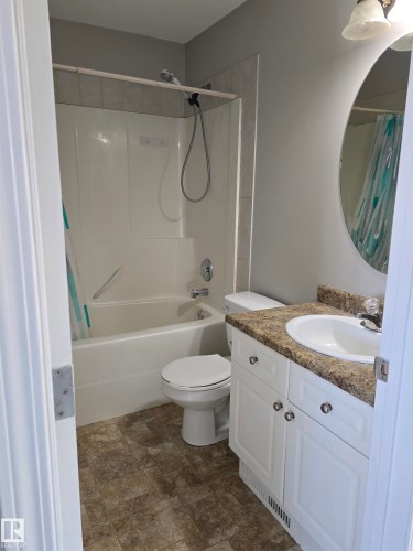 Bathroom featuring a white bathtub and shower combination with tile surround, white vanity with a light-toned countertop, integrated sink, and a circular mirror - 4120 47 Street, Drayton Valley, AB - Indoor Photo Showing Bathroom