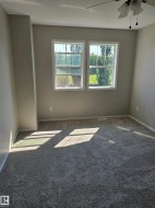 Carpeted interior space featuring two large windows, a ceiling fan with light fixture, light-toned walls, and white trim - 
