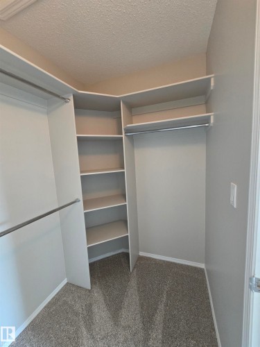 Walk-in closet featuring built-in shelving, two hanging rods, light gray walls, and textured carpet flooring - 4120 47 Street, Drayton Valley, AB - Indoor With Storage