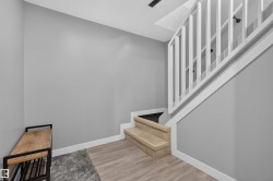 Staircase featuring wood-finish treads and a white balustrade, complemented by light gray walls and wood-finish flooring - 