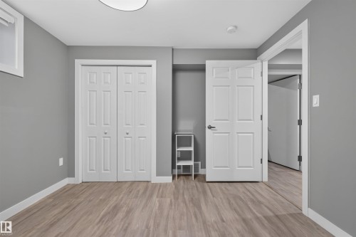 Room featuring neutral gray walls, wood-finish flooring, white trim, and a bi-fold closet with panel doors - 12136 135A Avenue Nw, Edmonton, AB - Indoor