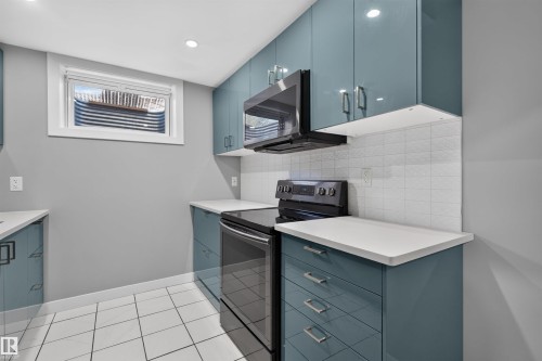 Modern kitchen featuring glossy teal cabinetry, white countertops, and a white subway tile backsplash - 12136 135A Avenue Nw, Edmonton, AB - Indoor Photo Showing Kitchen