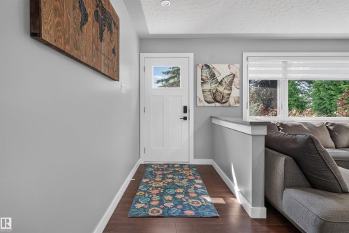 Entryway featuring dark wood-finish flooring, a contemporary white door with frosted glass paneling, and a large window providing outdoor views - 12136 135A Avenue Nw, Edmonton, AB - Indoor Photo Showing Other Room