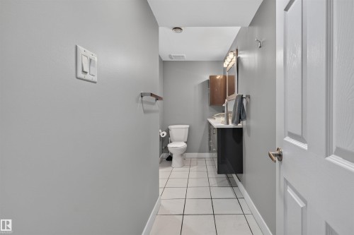 Bathroom featuring a white toilet, contemporary vanity with a dark cabinet, square vessel sink, and a framed mirror with a multi-bulb light fixture - 12136 135A Avenue Nw, Edmonton, AB - Indoor Photo Showing Bathroom