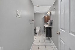 Bathroom featuring a white toilet, contemporary vanity with a dark cabinet, square vessel sink, and a framed mirror with a multi-bulb light fixture - 