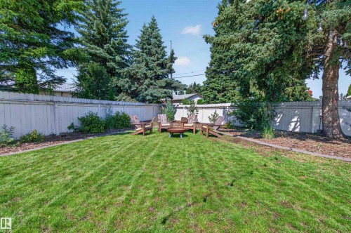 Spacious grass lawn with a fire pit area, surrounded by a privacy fence and mature trees - 12136 135A Avenue Nw, Edmonton, AB - Outdoor With Backyard