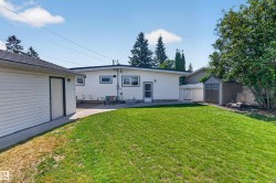 Expansive rear yard featuring a manicured lawn, a detached garage with vinyl siding, and a white picket fence - 