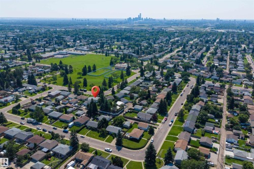 Aerial perspective showcasing a residential neighborhood with tree-lined streets, a large green space, and distant city skyline - 12136 135A Avenue Nw, Edmonton, AB - Outdoor With View