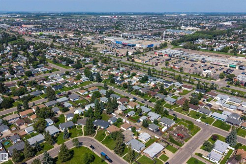 Aerial view of a residential area with varied housing styles and mature trees, featuring a commercial district in the background with multiple retail buildings and parking lots - 12136 135A Avenue Nw, Edmonton, AB - Outdoor With View