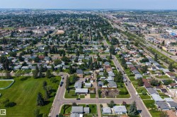 Expansive aerial perspective showcasing a residential neighborhood with detached homes, mature trees, and a manicured green space - 