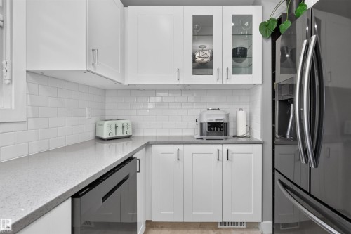 Kitchen featuring white shaker-style cabinetry, light-toned countertops, white subway tile backsplash, and a built-in stainless steel appliance - 12136 135A Avenue Nw, Edmonton, AB - Indoor Photo Showing Kitchen