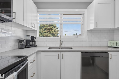 Kitchen featuring a stainless steel sink, white subway tile backsplash, white shaker-style cabinetry with matte black hardware, and light gray countertops - 12136 135A Avenue Nw, Edmonton, AB - Indoor Photo Showing Kitchen With Double Sink