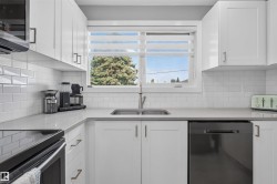 Kitchen featuring a stainless steel sink, white subway tile backsplash, white shaker-style cabinetry with matte black hardware, and light gray countertops - 