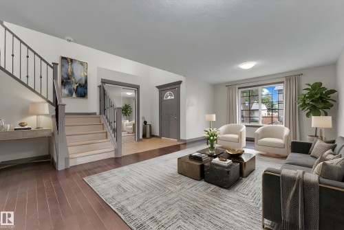 Spacious living area featuring wood-finish flooring, a prominent staircase with iron railings, a large window with window treatments, recessed lighting, and a front entry door with an arched window accent - 11817 37 Street Nw, Edmonton, AB - Indoor Photo Showing Living Room