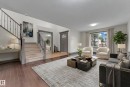 Spacious living area featuring wood-finish flooring, a prominent staircase with iron railings, a large window with window treatments, recessed lighting, and a front entry door with an arched window accent - 11817 37 Street Nw, Edmonton, AB  - Indoor Photo Showing Living Room 