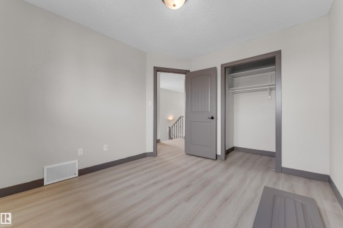 Spacious room featuring light wood-finish flooring, neutral gray walls, a built-in closet with shelving and hanging rod, and a coordinating gray paneled door - 11817 37 Street Nw, Edmonton, AB - Indoor Photo Showing Other Room