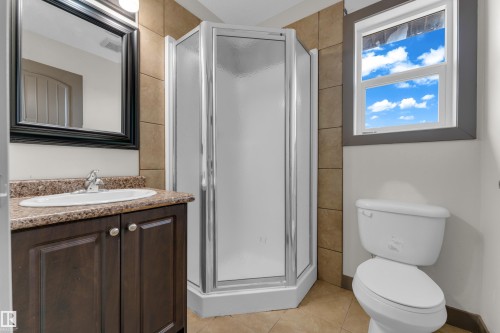 Bathroom featuring a dark wood vanity with an oval sink, a framed mirror, a corner shower, and a window with gray trim - 11817 37 Street Nw, Edmonton, AB - Indoor Photo Showing Bathroom