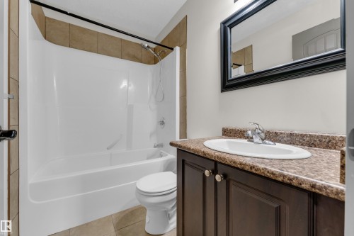 Bathroom vanity featuring a dark wood-finish cabinet with double doors and knob hardware, paired with a speckled countertop and an oval undermount sink - 11817 37 Street Nw, Edmonton, AB - Indoor Photo Showing Bathroom