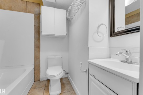 Bathroom featuring a white vanity with integrated sink, chrome faucet, wall-mounted mirror, and white toilet - 11817 37 Street Nw, Edmonton, AB - Indoor Photo Showing Bathroom