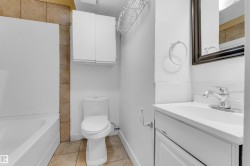 Bathroom featuring a white vanity with integrated sink, chrome faucet, wall-mounted mirror, and white toilet - 