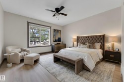 Spacious bedroom featuring wood-finish flooring, a large window with exterior tree views, a ceiling fan, and ample wall space - 