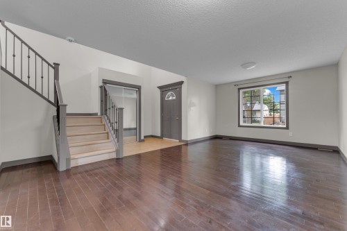 Spacious interior featuring dark wood-finish flooring, a prominent staircase with iron balusters, a front entry door with an arched window insert, a large multi-pane window, and light-toned walls with contrasting trim - 11817 37 Street Nw, Edmonton, AB - Indoor